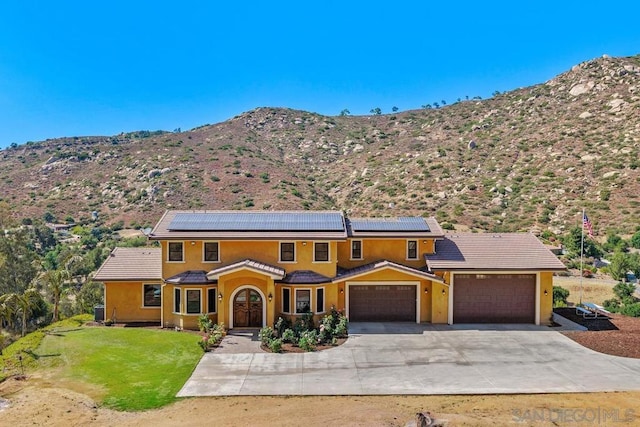 view of front of house with solar panels, a front lawn, a mountain view, and a garage