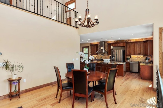 dining room with a high ceiling, sink, a chandelier, and light hardwood / wood-style flooring