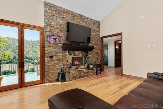 living room featuring high vaulted ceiling, a stone fireplace, hardwood / wood-style floors, french doors, and a mountain view