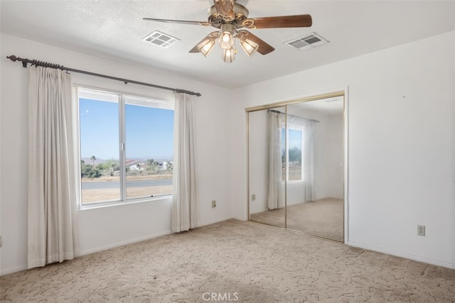 unfurnished bedroom featuring light carpet, a closet, ceiling fan, and multiple windows