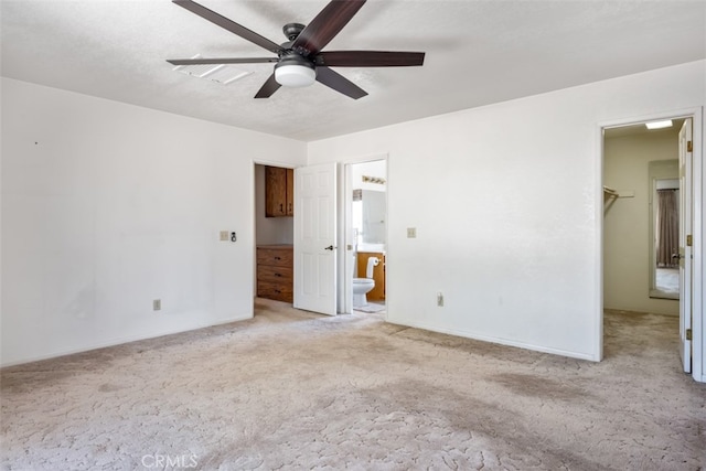 unfurnished bedroom with light carpet, ensuite bath, ceiling fan, and a walk in closet