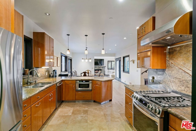 kitchen with wall chimney range hood, stainless steel appliances, sink, hanging light fixtures, and kitchen peninsula