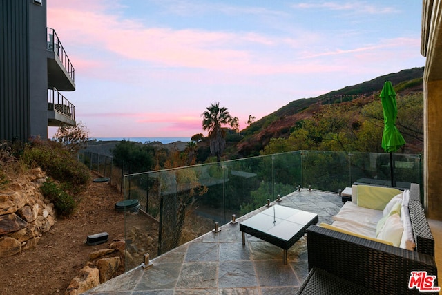 patio terrace at dusk with a mountain view, a balcony, and outdoor lounge area