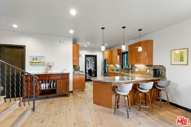 kitchen with kitchen peninsula, sink, stainless steel refrigerator, hanging light fixtures, and light wood-type flooring