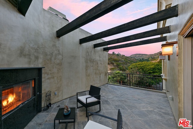 patio terrace at dusk featuring a mountain view and exterior fireplace