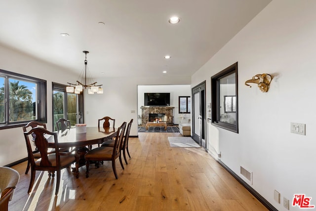 dining area with a stone fireplace, a chandelier, and light hardwood / wood-style flooring