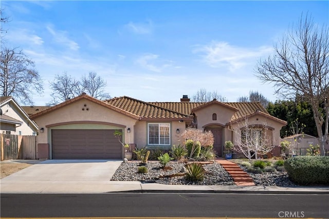 mediterranean / spanish house featuring stucco siding, fence, concrete driveway, an attached garage, and a chimney