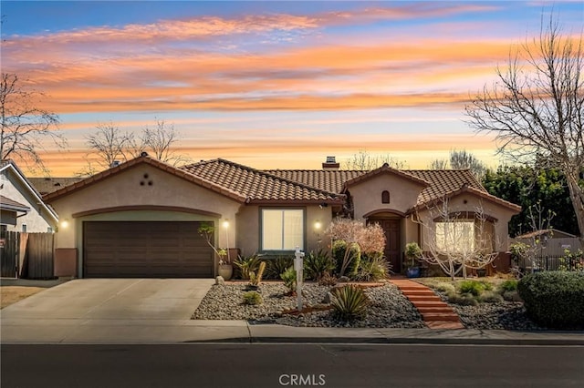 mediterranean / spanish-style home with fence, a tiled roof, concrete driveway, stucco siding, and a garage