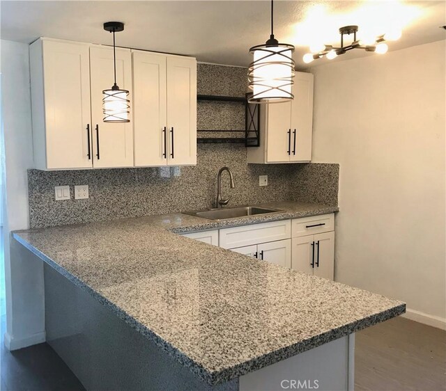 kitchen with kitchen peninsula, hanging light fixtures, sink, tasteful backsplash, and white cabinets