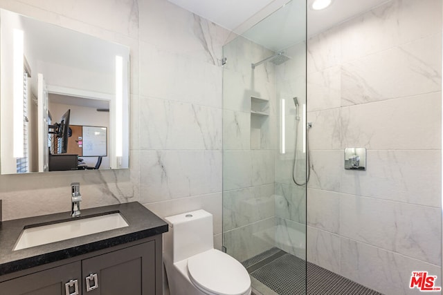 bathroom featuring a tile shower, vanity, tile walls, and toilet