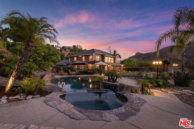 pool at dusk with an in ground hot tub, a mountain view, and a patio