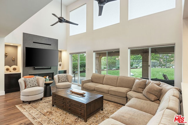 living room with a towering ceiling, light wood-type flooring, and ceiling fan