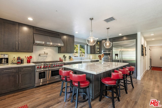 kitchen featuring a center island, dark wood-type flooring, wall chimney exhaust hood, premium appliances, and dark brown cabinets