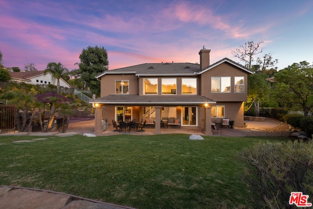 back house at dusk with a lawn and a patio