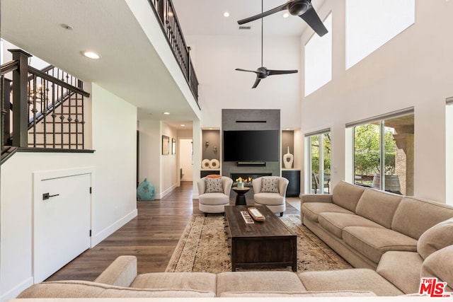 living room with ceiling fan, dark wood-type flooring, and a high ceiling