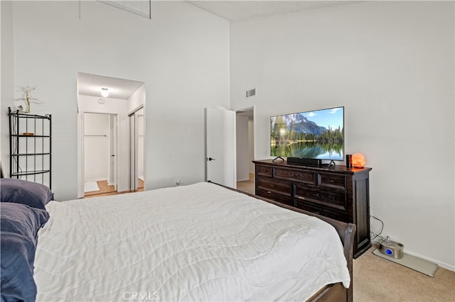 bedroom featuring light colored carpet, a closet, ensuite bath, and a high ceiling