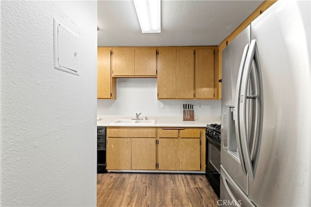 kitchen featuring a textured ceiling, light hardwood / wood-style floors, sink, black range with gas stovetop, and stainless steel fridge