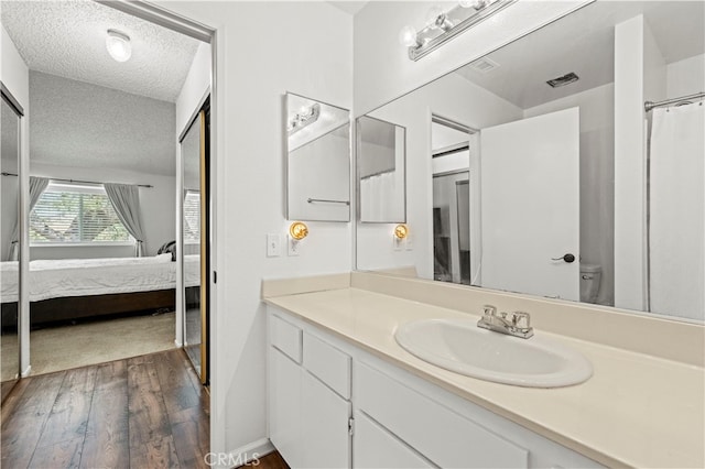 bathroom with wood-type flooring, a textured ceiling, toilet, vanity, and curtained shower