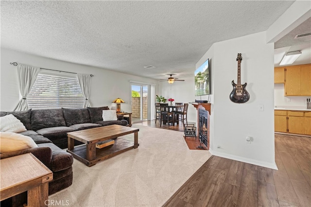 living room featuring light wood-type flooring, ceiling fan, and a textured ceiling