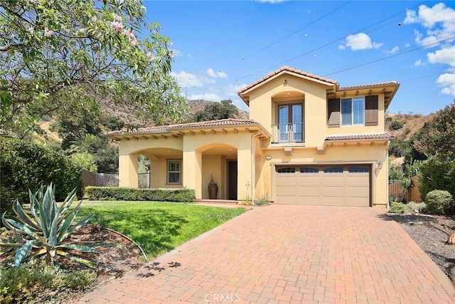 mediterranean / spanish-style house with decorative driveway, fence, an attached garage, a balcony, and a tiled roof