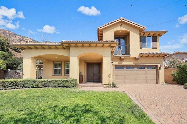 mediterranean / spanish house featuring a front yard, a balcony, fence, and stucco siding