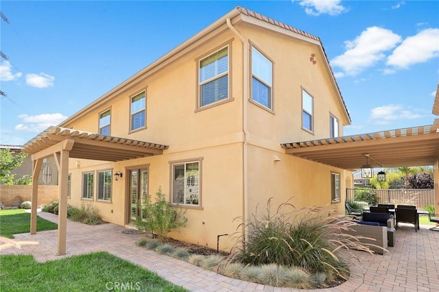 rear view of house with stucco siding, a pergola, a patio, and fence