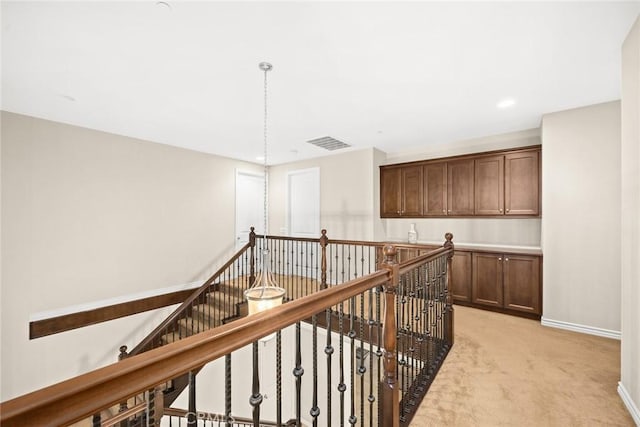 hall with an upstairs landing, visible vents, light carpet, and baseboards