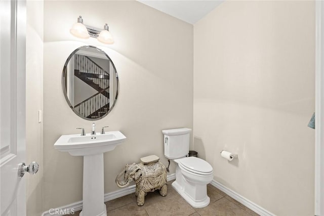 half bathroom featuring a sink, baseboards, toilet, and tile patterned flooring