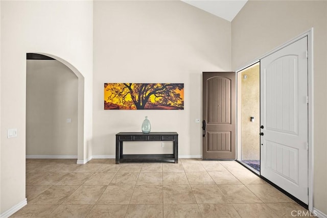 tiled foyer featuring baseboards, arched walkways, and a towering ceiling