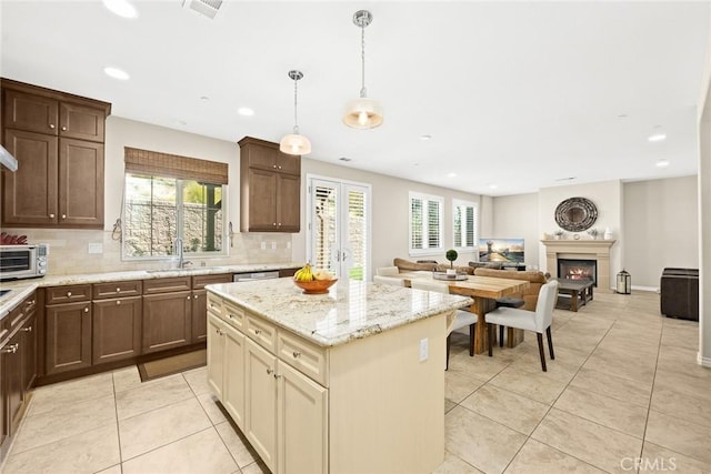 kitchen featuring backsplash, a kitchen island, a lit fireplace, light tile patterned floors, and a sink