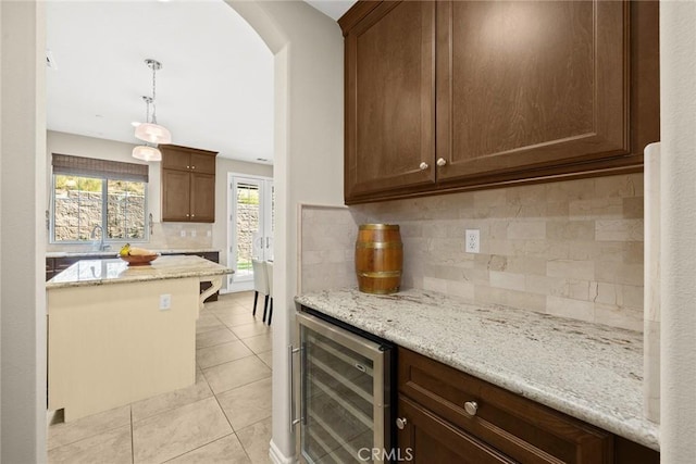 kitchen featuring wine cooler, light tile patterned flooring, light stone countertops, and decorative light fixtures