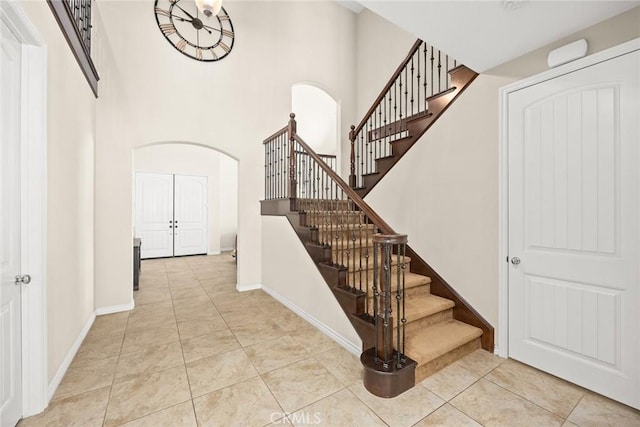 staircase with arched walkways, tile patterned floors, a high ceiling, and baseboards