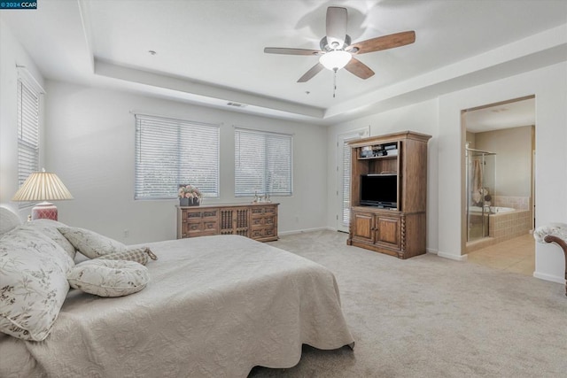 bedroom with connected bathroom, a tray ceiling, light carpet, and ceiling fan