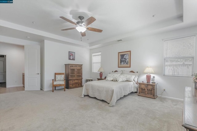 bedroom featuring multiple windows, a tray ceiling, ceiling fan, and light colored carpet