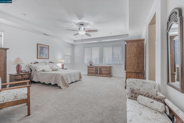 bedroom with a raised ceiling, light carpet, and ceiling fan