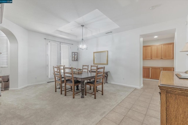 dining space with light carpet, a tray ceiling, and a chandelier