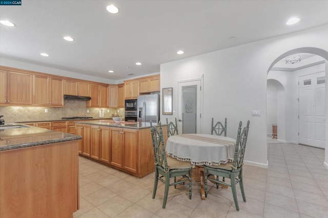 kitchen featuring appliances with stainless steel finishes, dark stone counters, light tile patterned floors, and tasteful backsplash