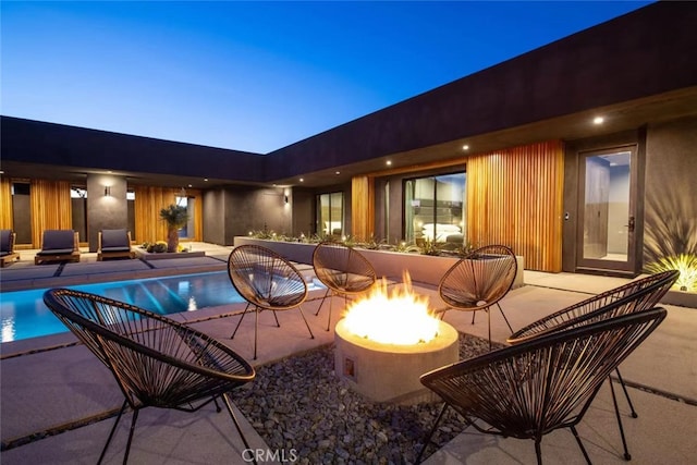 pool at dusk featuring a fire pit and a patio area