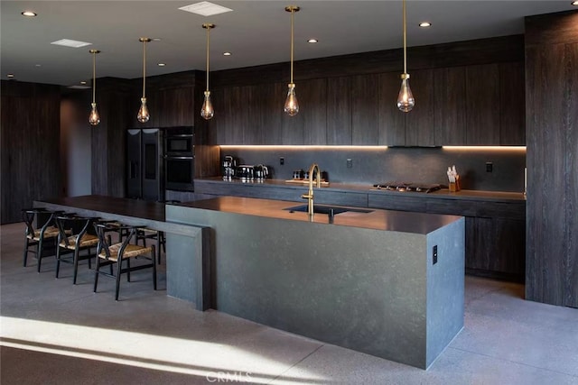 kitchen with hanging light fixtures, sink, tasteful backsplash, a kitchen island with sink, and appliances with stainless steel finishes