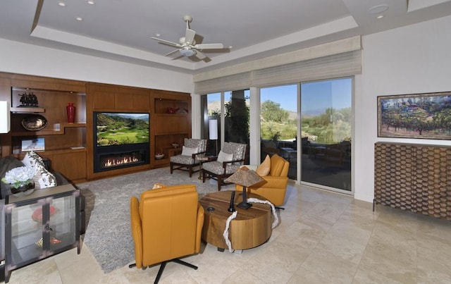 living room with ceiling fan, built in features, and a raised ceiling