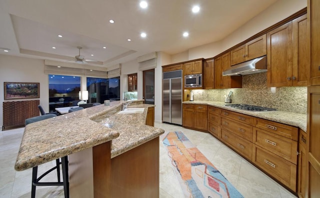 kitchen featuring a large island, a tray ceiling, a breakfast bar, and built in appliances