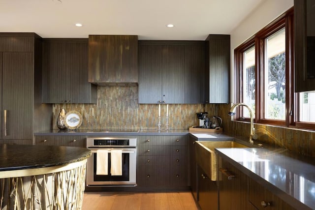 kitchen featuring dark brown cabinetry, sink, oven, and wall chimney exhaust hood