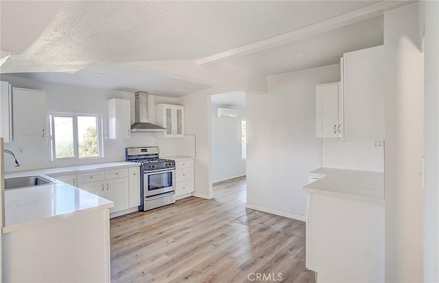 kitchen featuring white cabinetry, sink, wall chimney exhaust hood, stainless steel gas range, and tasteful backsplash