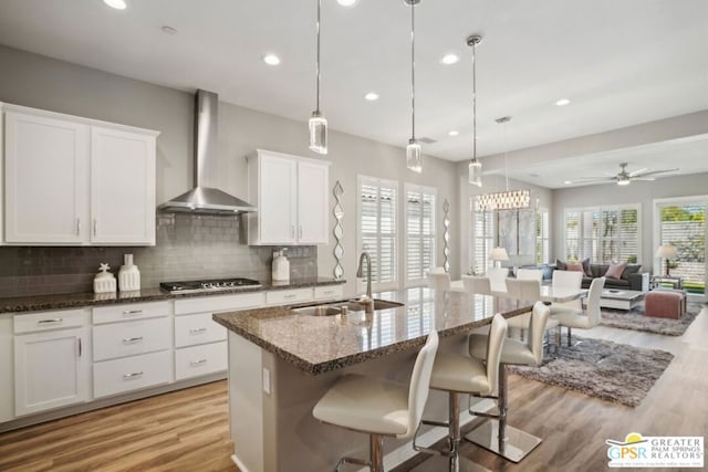 kitchen featuring sink, wall chimney exhaust hood, pendant lighting, and a center island with sink