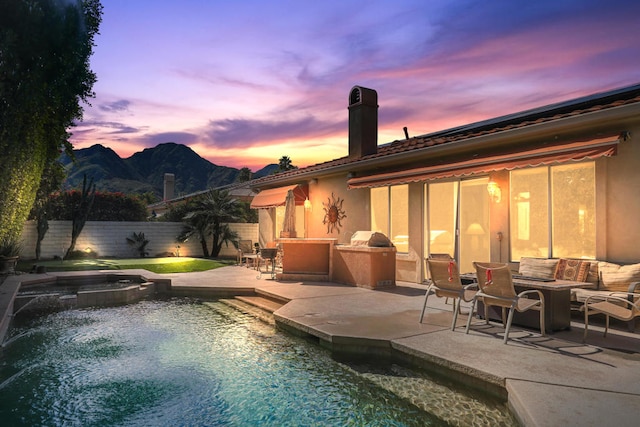 pool at dusk featuring a mountain view, an in ground hot tub, and a patio area