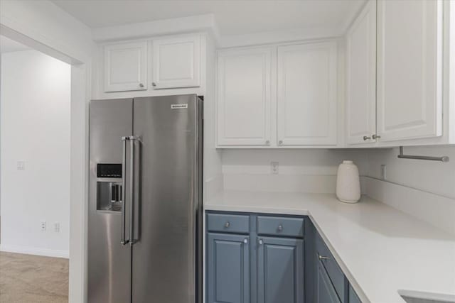 kitchen featuring white cabinets, blue cabinets, light carpet, and stainless steel fridge