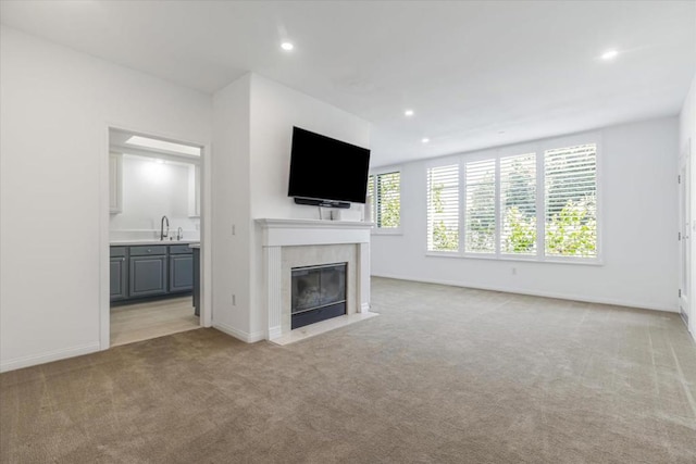 unfurnished living room with light colored carpet, a tile fireplace, and sink