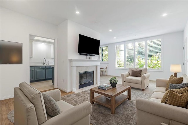 living room featuring sink, light hardwood / wood-style flooring, and a tiled fireplace