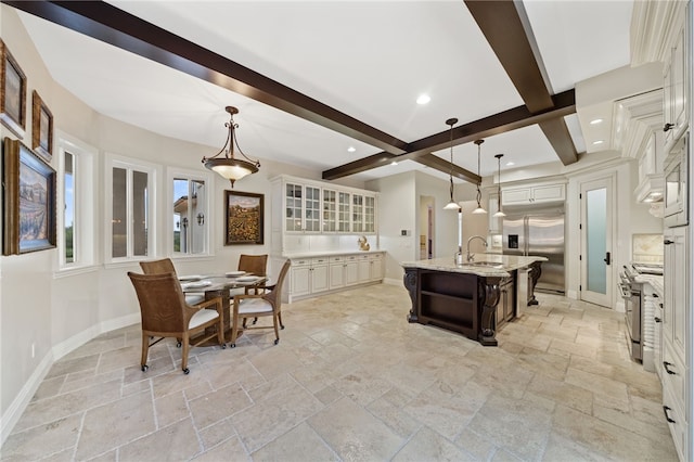 kitchen featuring an island with sink, stainless steel appliances, beamed ceiling, and hanging light fixtures