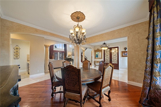 dining area with wood-type flooring, crown molding, an inviting chandelier, and ornate columns